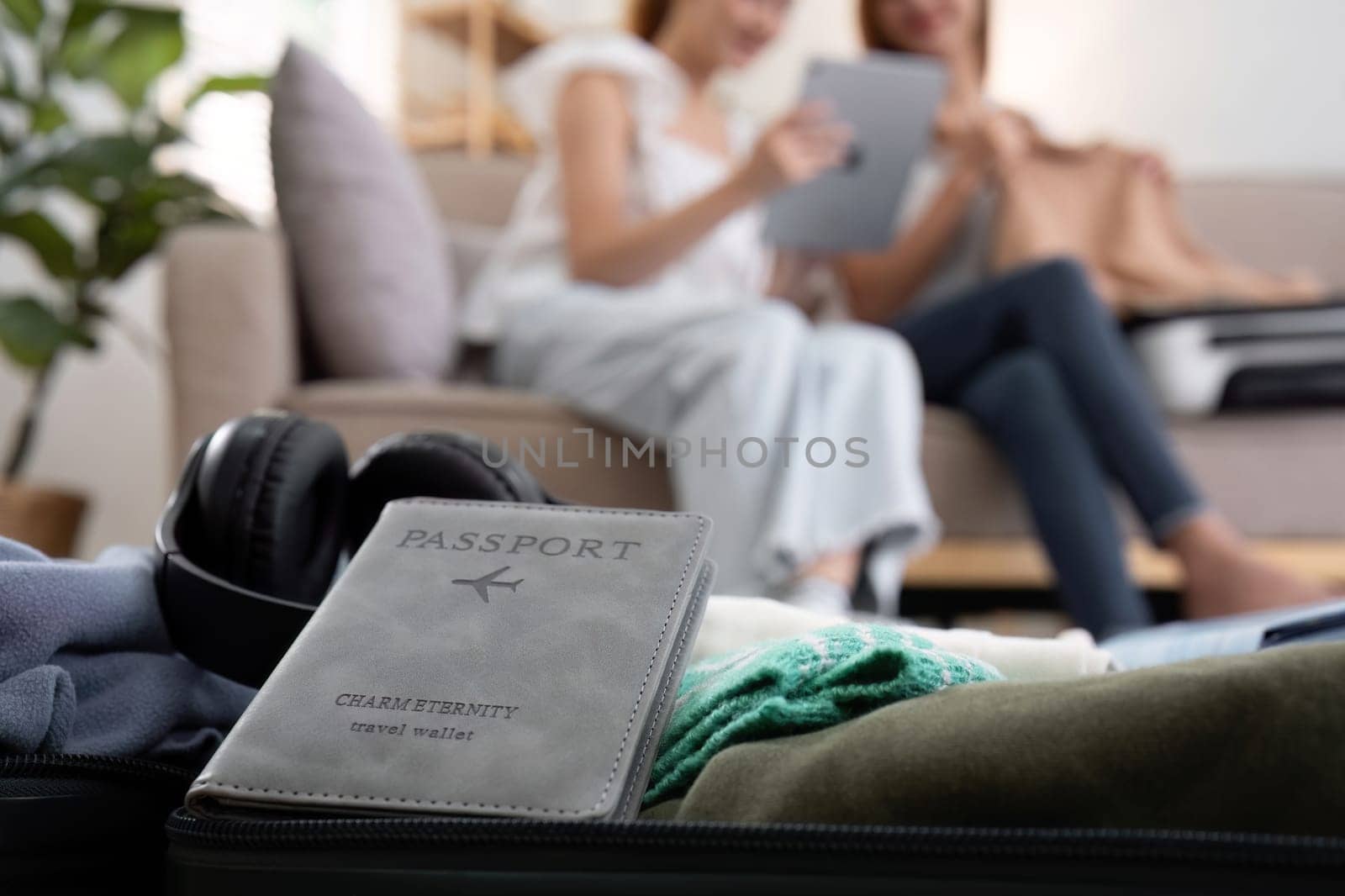 Close-up of passports placed on suitcases with background of two young female friends packing suitcases with clothes in preparation for the weekend..