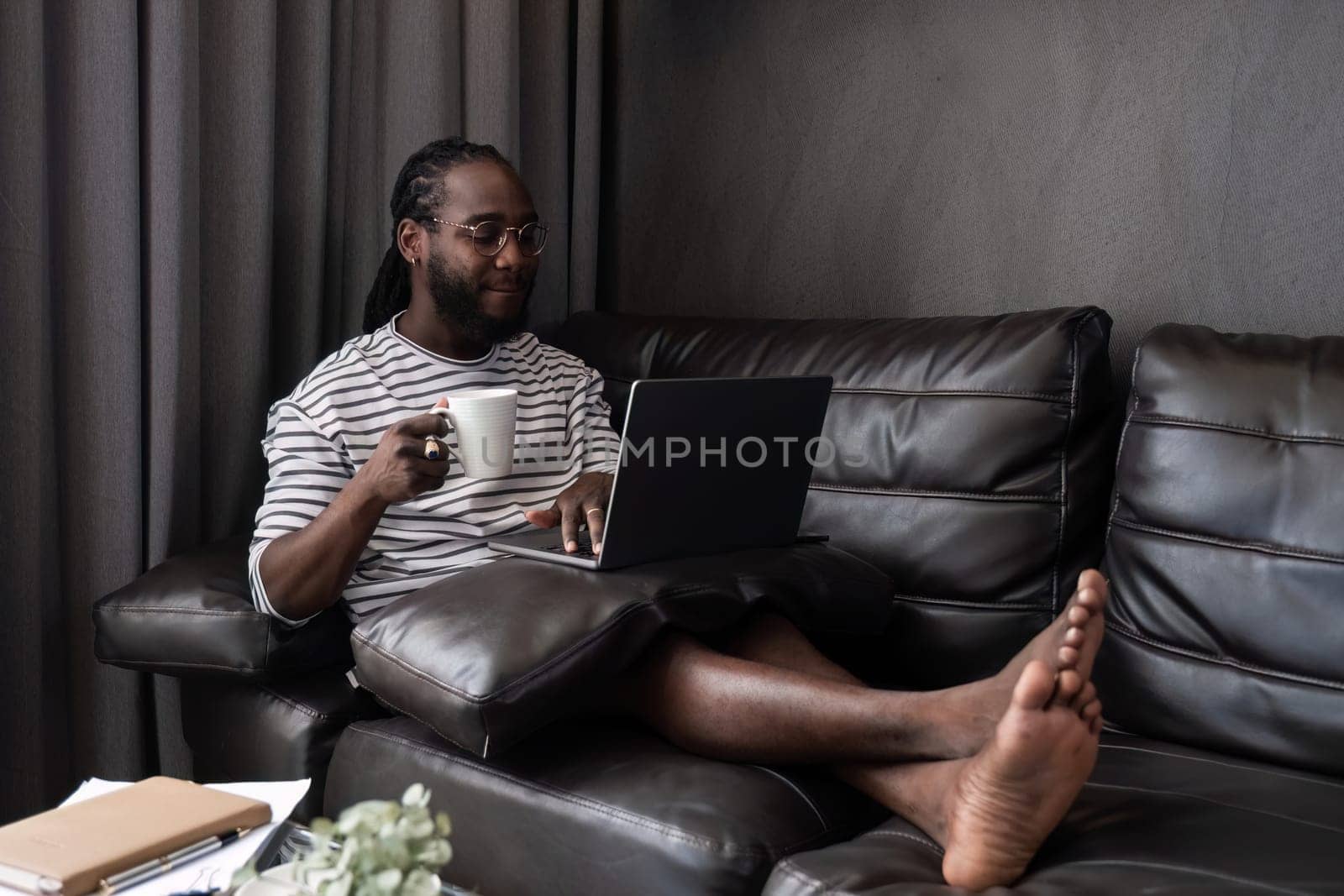 Young African American businessman spends his weekend working from home using his laptop in the living room. by wichayada