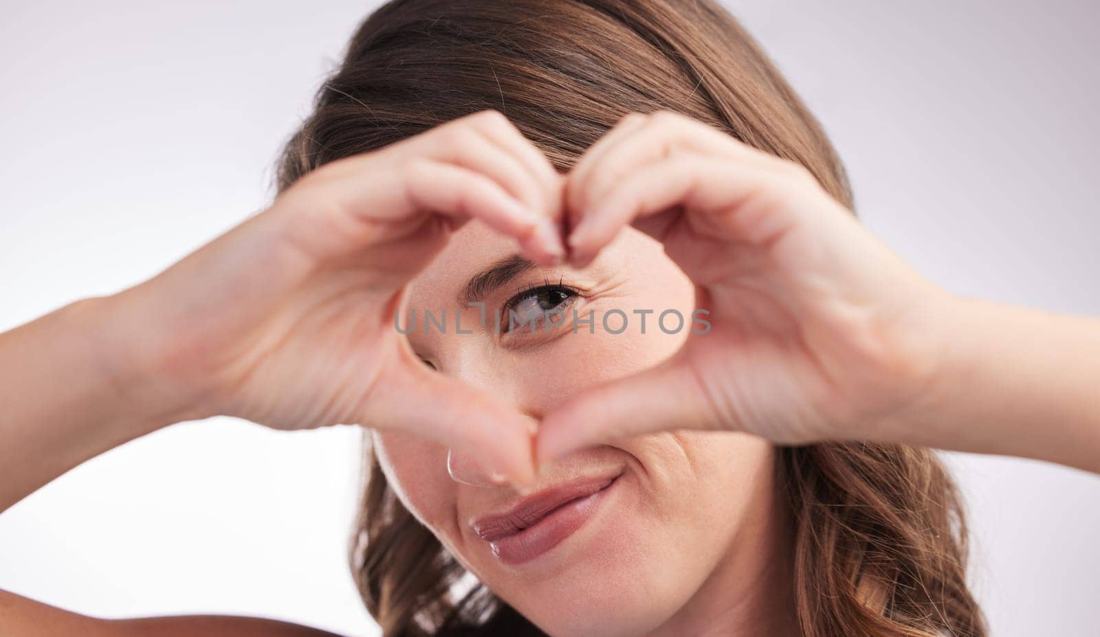 Woman, heart hands and sign for love in portrait, donation or charity with wellness and care on white background. Emoji, shape and romance gesture with thank you, feedback or reaction in studio.