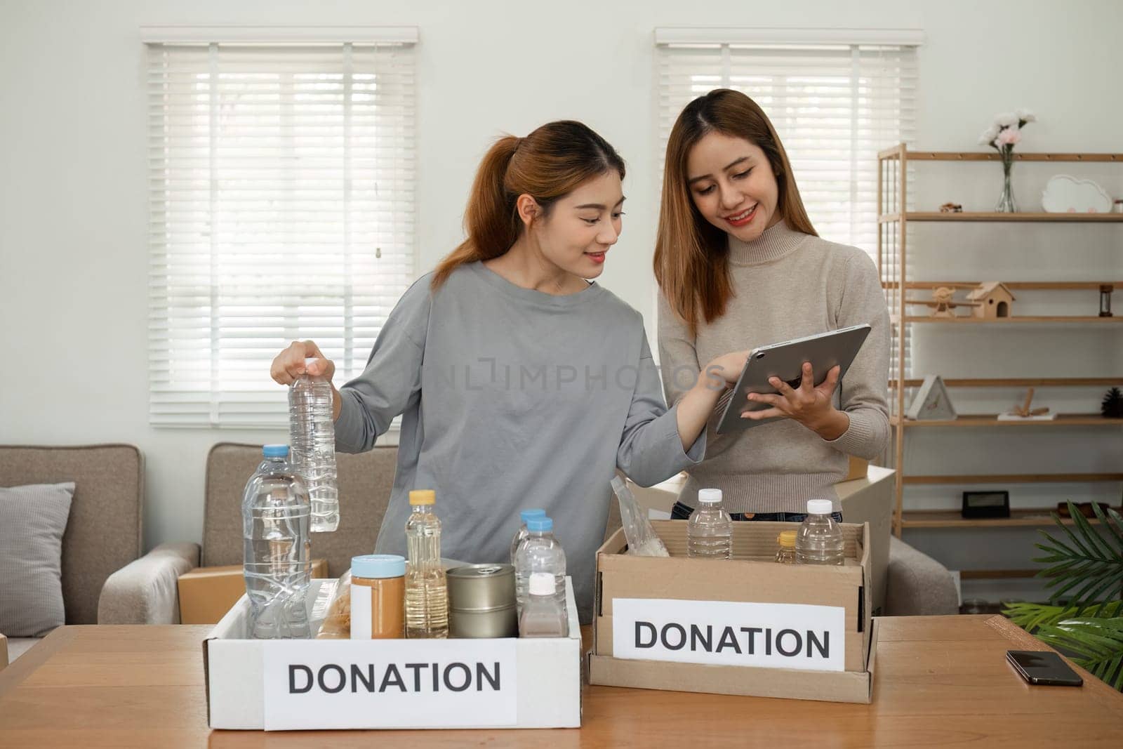 Two young female volunteers help pack food into donation boxes and prepare to donate them to charity. by wichayada