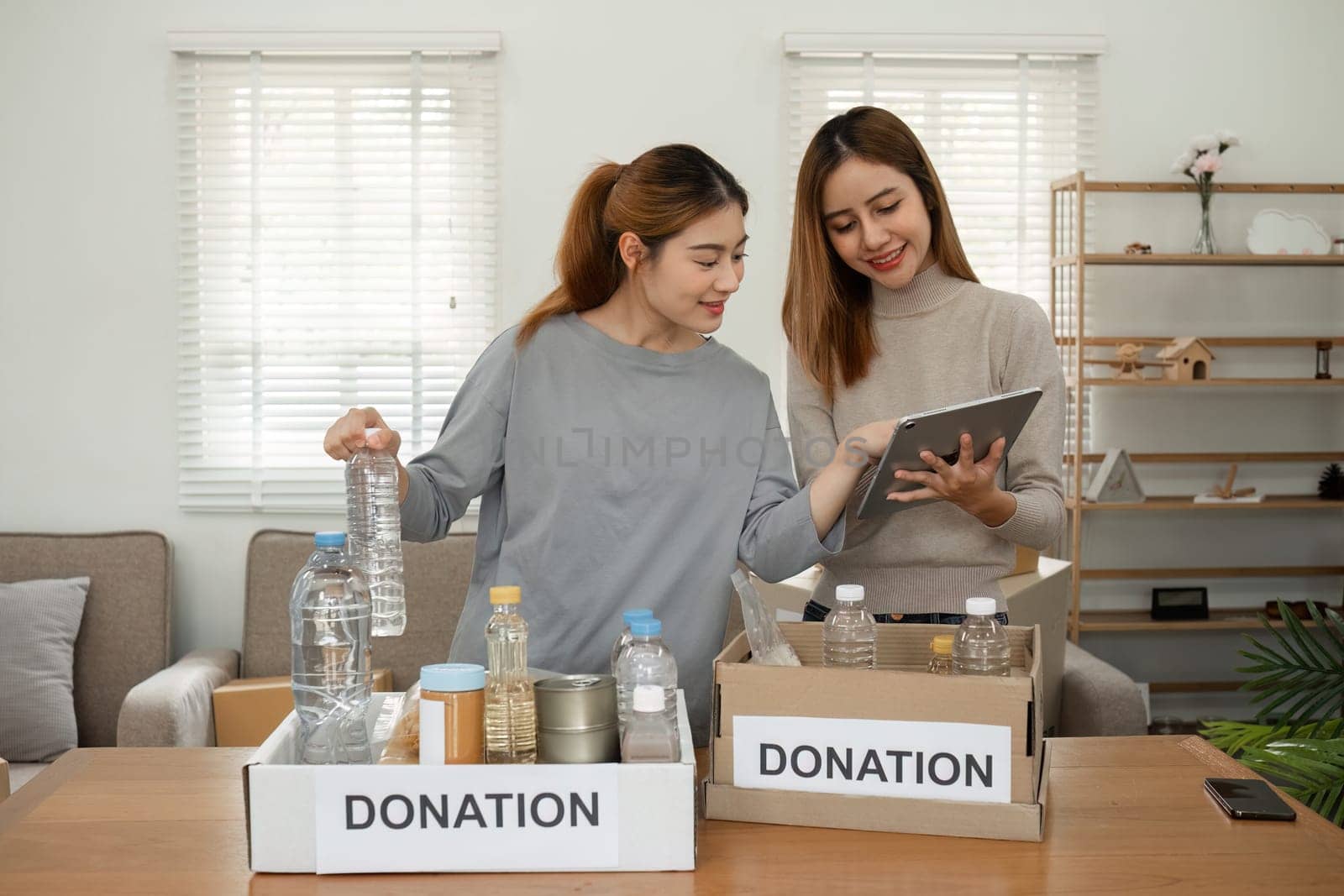 Two young female volunteers help pack food into donation boxes and prepare to donate them to charity..