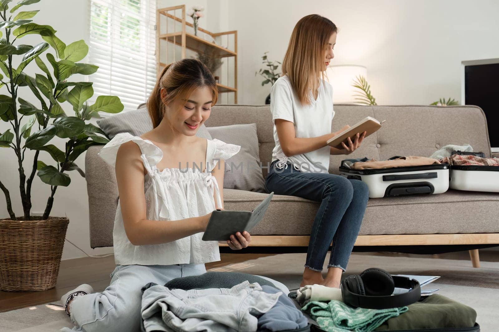 Two young female friends pack a suitcase with clothes and travel passports in preparation for a weekend away. by wichayada