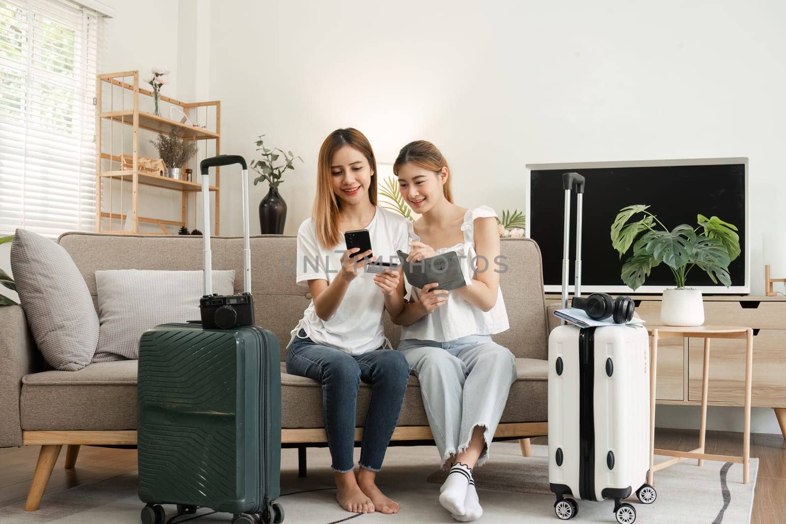 Two young female friends pack a suitcase with clothes and travel passports in preparation for a weekend away. by wichayada