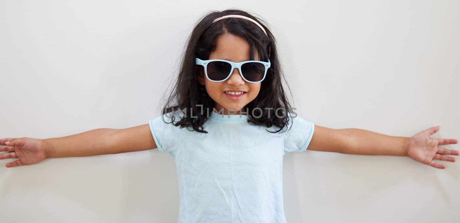 Girl, child and smile with sunglasses by wall for summer, holiday and playful at family home. Kid, excited and happy with eyewear, games and fashion with trendy style, growth and development at house.