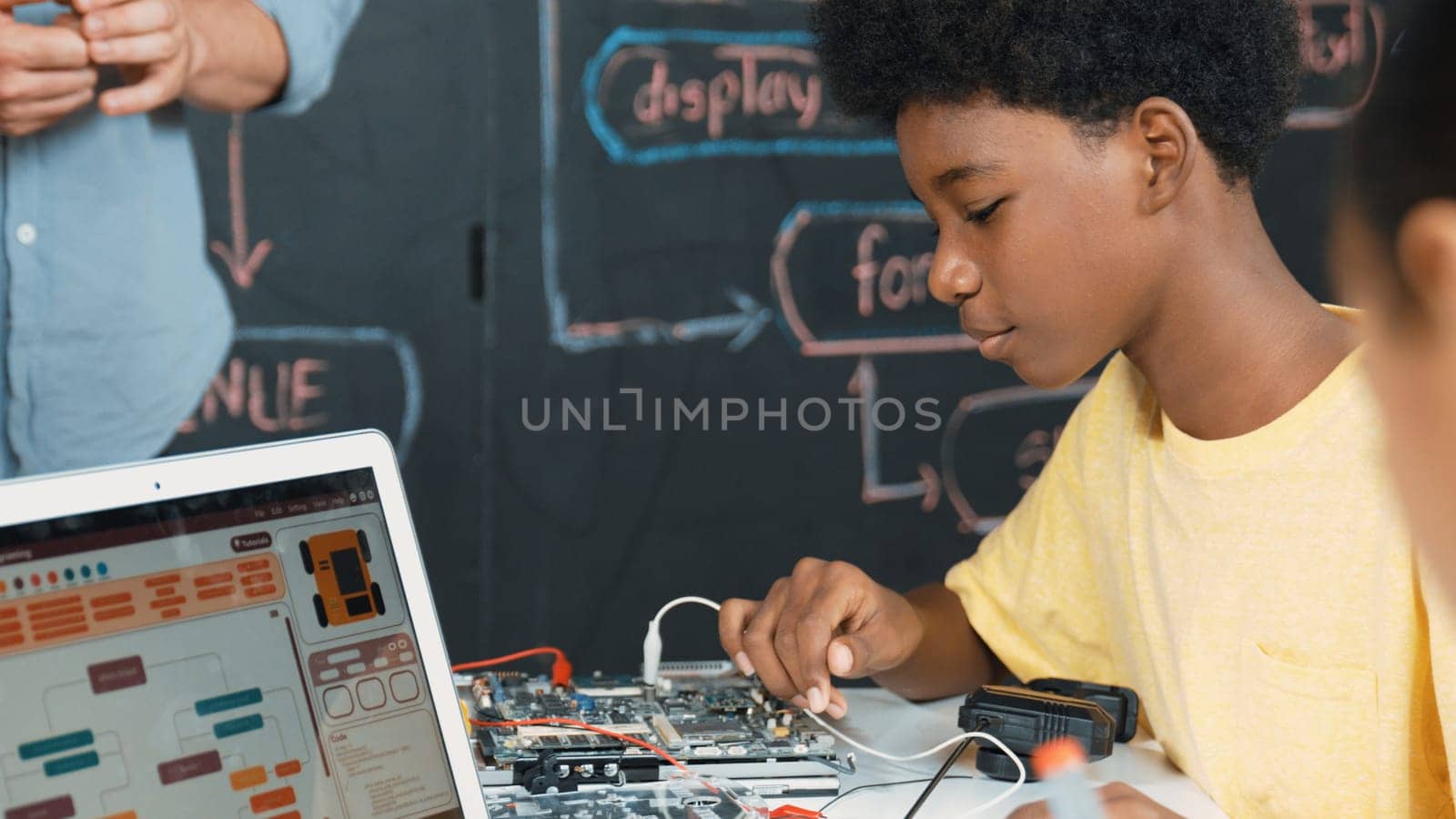 Cute african boy learning to use electronic tool while laptop display code while teacher talking about writing engineering prompt. Diverse children coding program to fixing car model. Edification.