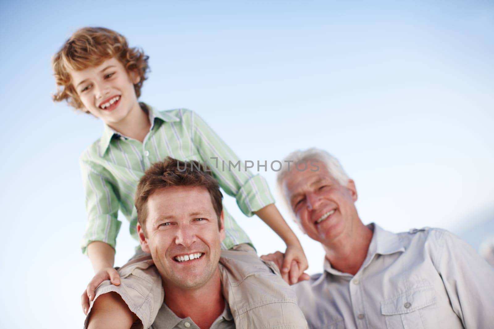 Portrait of grandfather, father and child by blue sky for bonding, relationship and relax together. Family, generations and grandpa, dad and young boy on shoulders for holiday, vacation and weekend by YuriArcurs