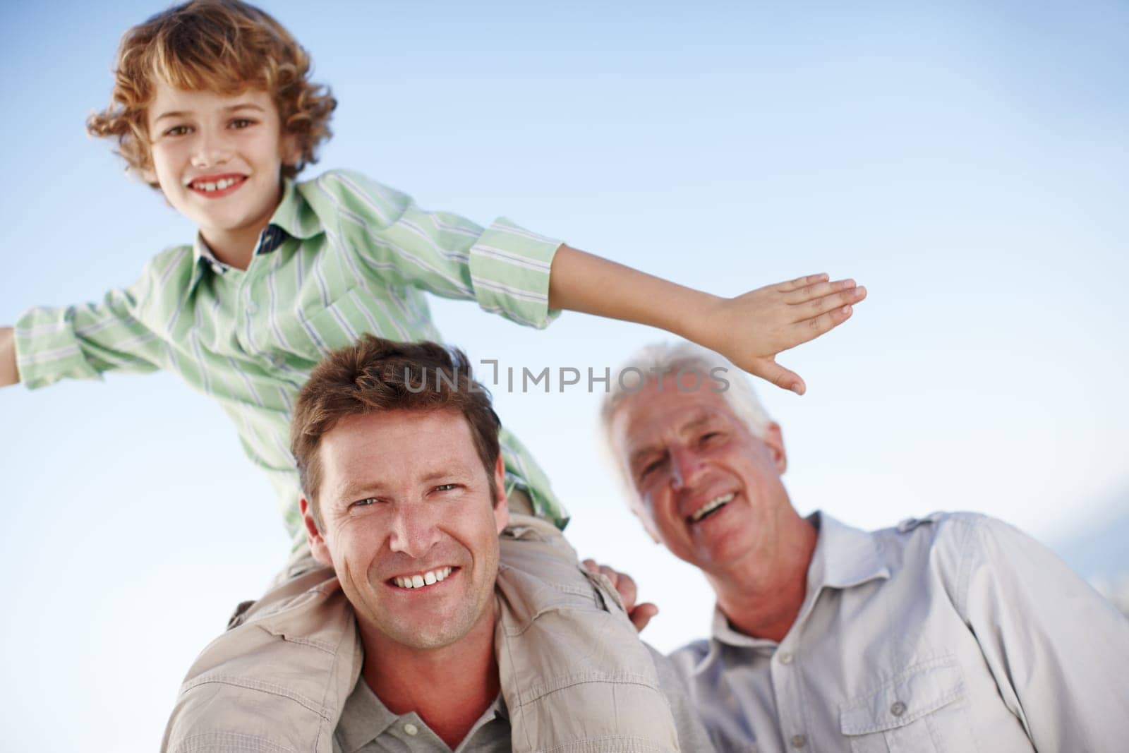 Portrait of grandpa, father and child by blue sky for bonding, relationship and relax together. Family, fun and grandfather, dad and young boy on shoulders for holiday, vacation and weekend outdoors.
