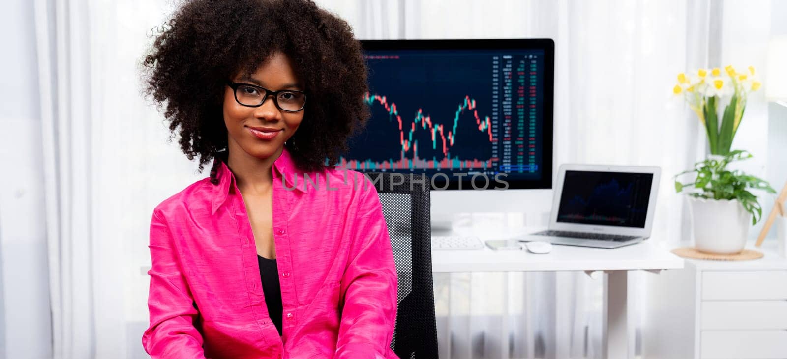 Analytical young African American businesswoman, a specialist in successful stock exchange trading, against dynamic data graph displaying marketing trend analysis on screen. Tastemaker.