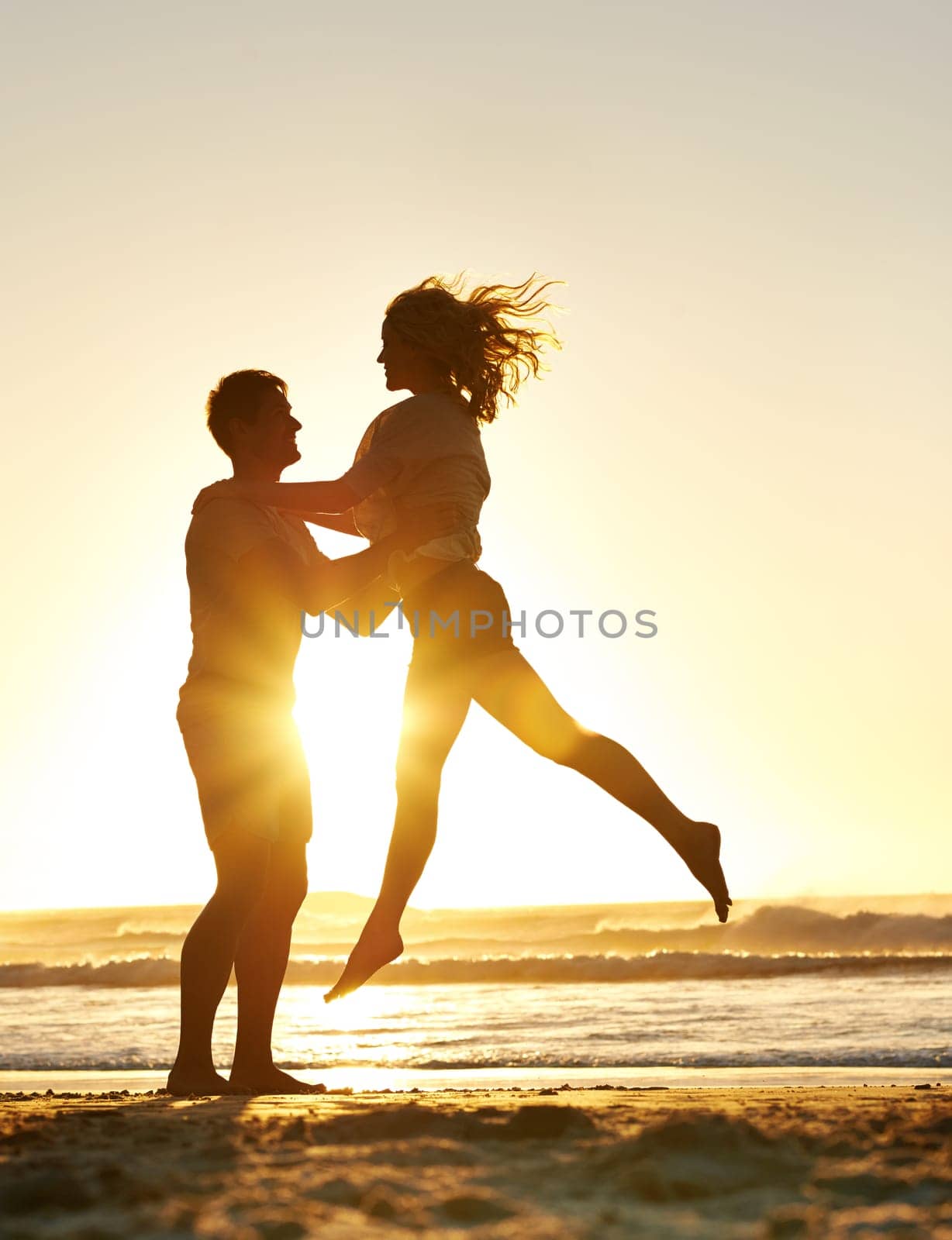 Lifting, sunset and couple with love at beach, ocean or sea for affection, bonding or for fun with soulmate. People, sunrise and romance for care together on vacation, holiday and travel in Australia.