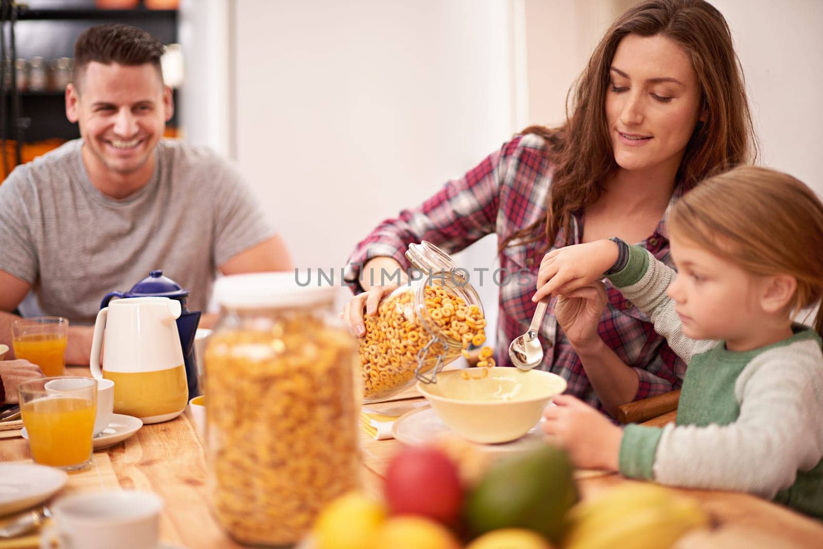 Mother, girl and breakfast with help for cereal, nutrition and health by table in house. Woman, kid and brunch together in home with dad by kitchen for wellness, eating and assistance with food.