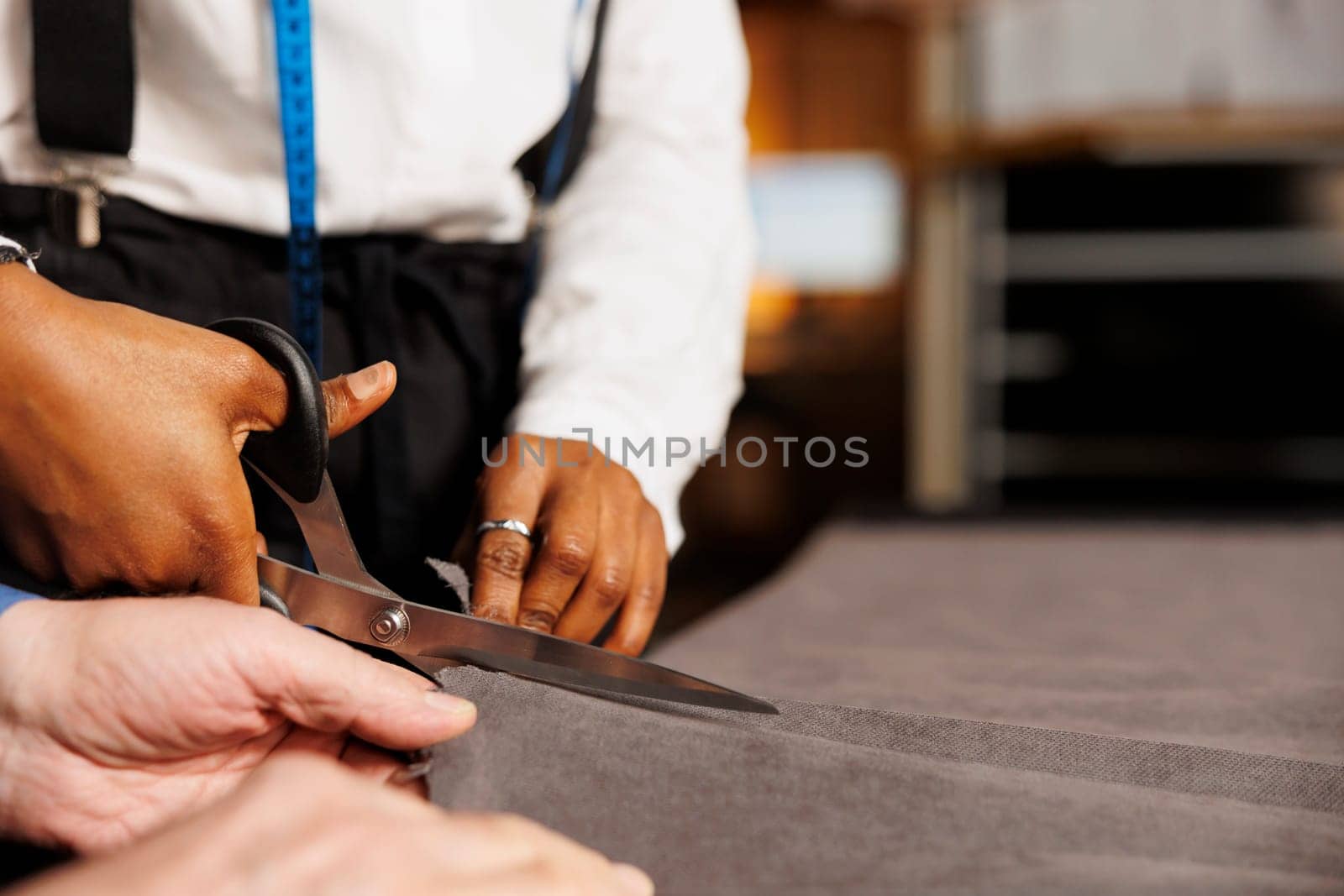 Extreme close up of seamstress using scissors to cut refined fabric material in professional atelier shop studio. Experienced dressmaker teaching tailor apprentice expert craftmanship