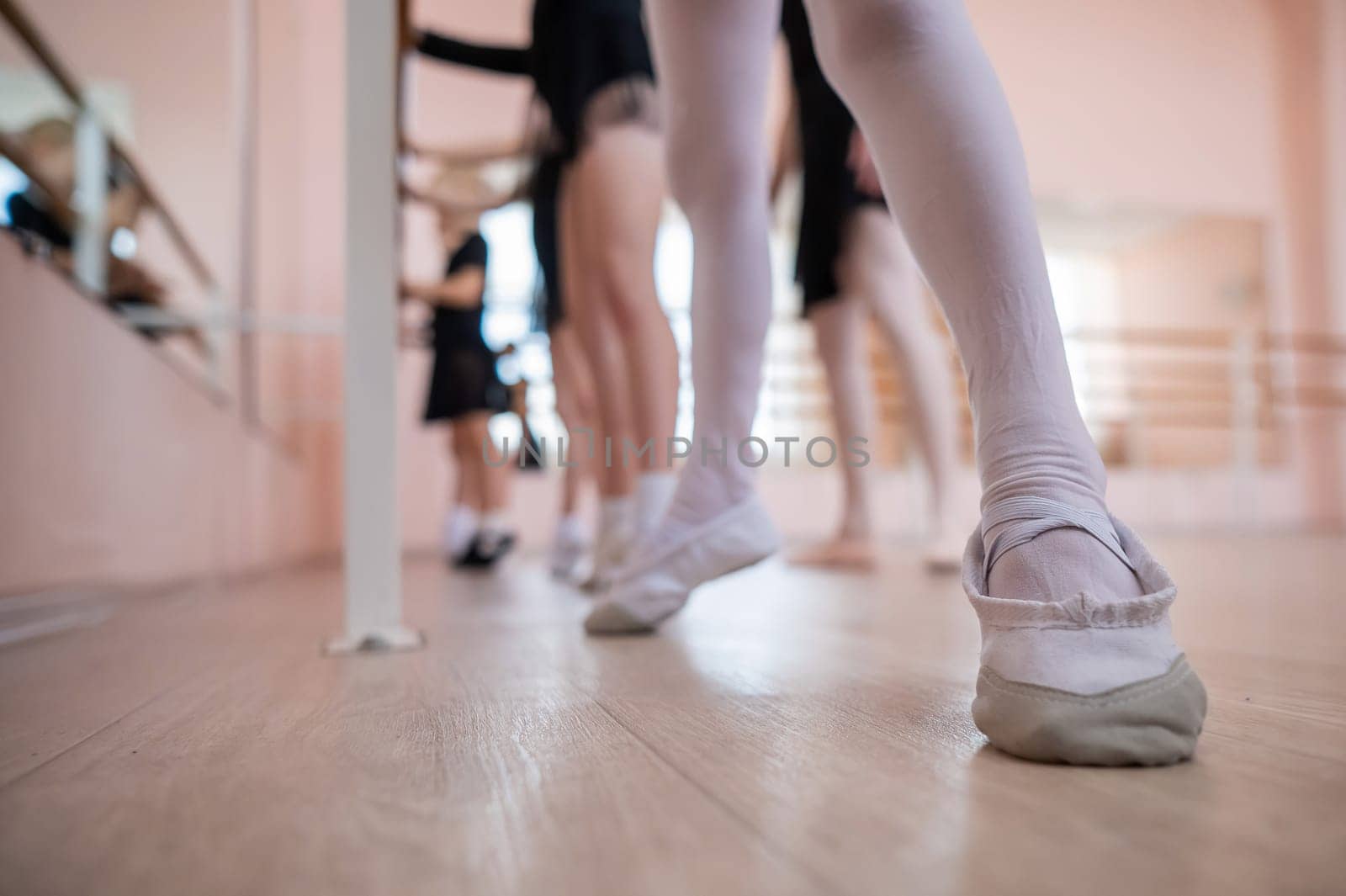 Little girls practice ballet at the barre. Close-up of young ballerinas' feet