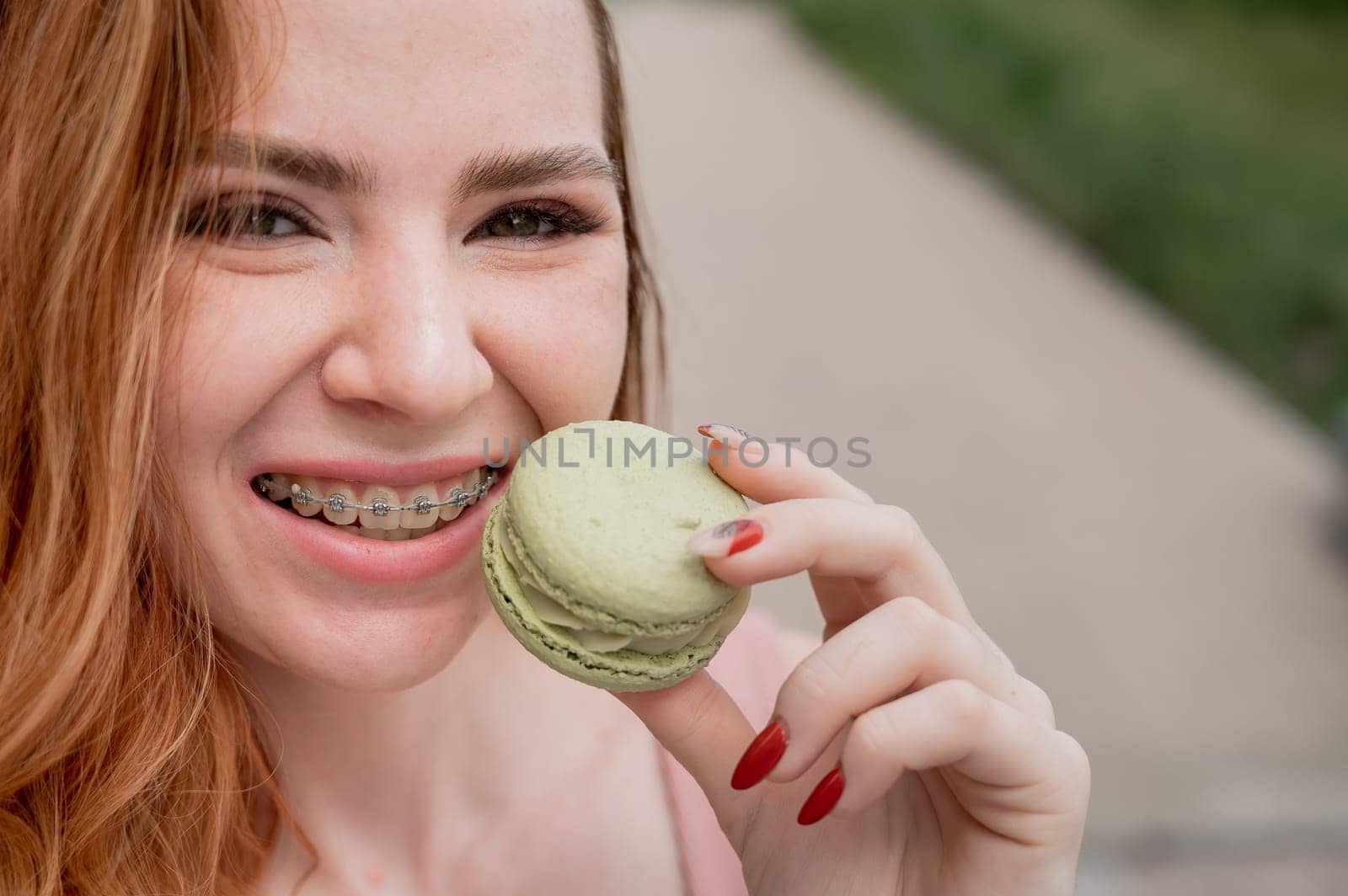 Young red-haired woman with braces eating macaron cake. by mrwed54