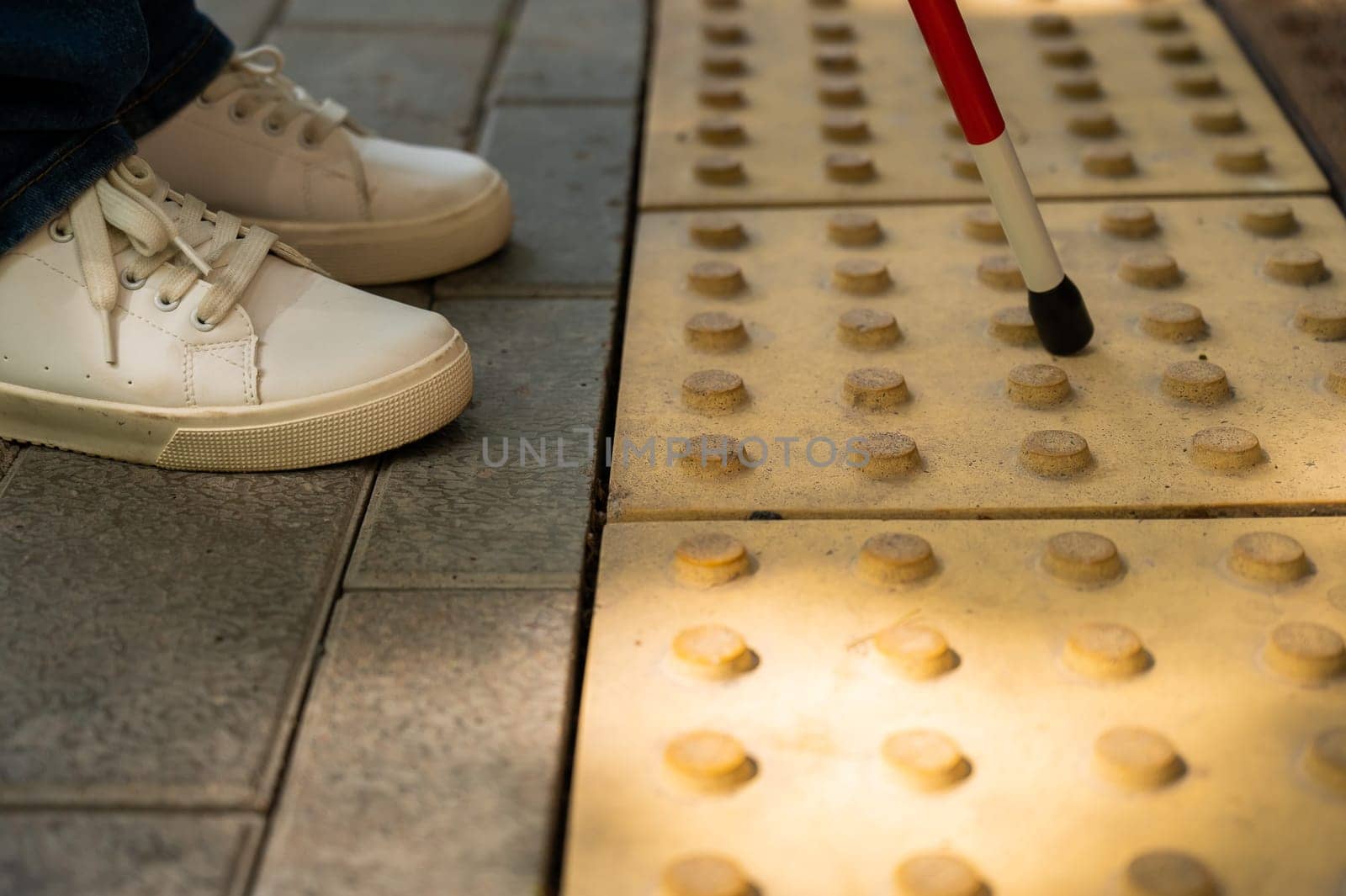 Close-up of female foot, walking stick and tactile tiles