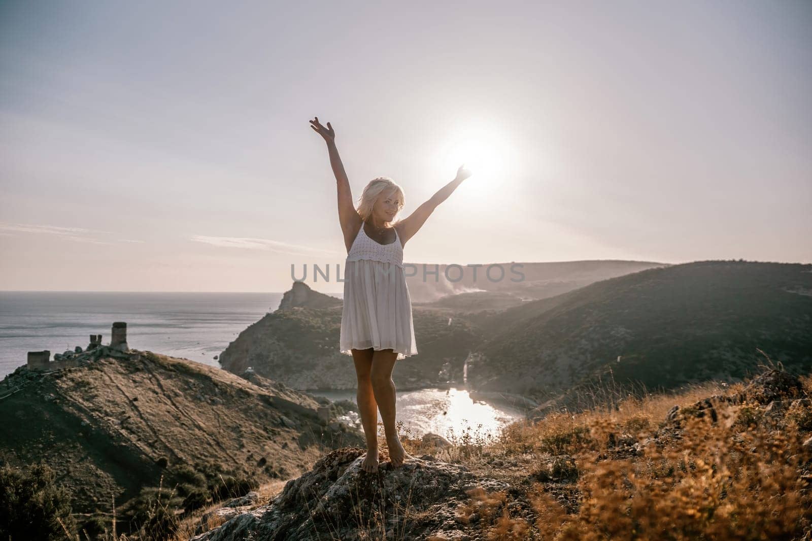 woman standing hill with her arms raised in the air, looking up at the sun. The scene is peaceful and serene, with the woman's expression conveying a sense of joy and happiness