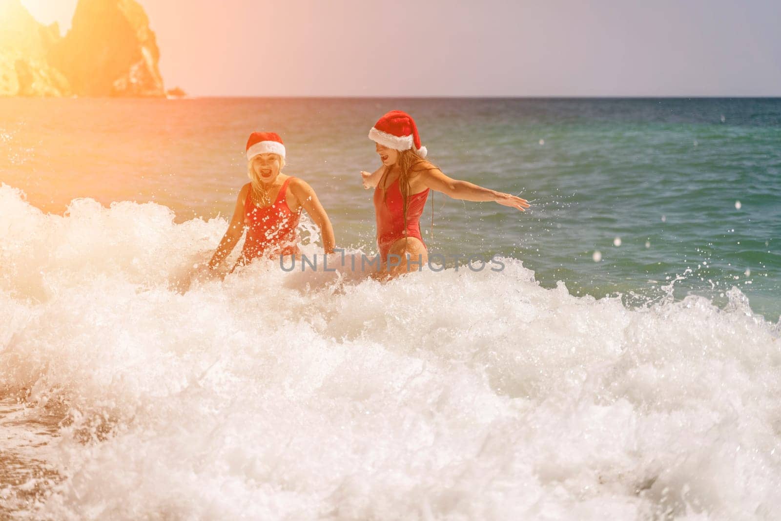 Women Santa hats ocean play. Seaside, beach daytime, enjoying beach fun. Two women in red swimsuits and Santa hats are enjoying themselves in the ocean waves