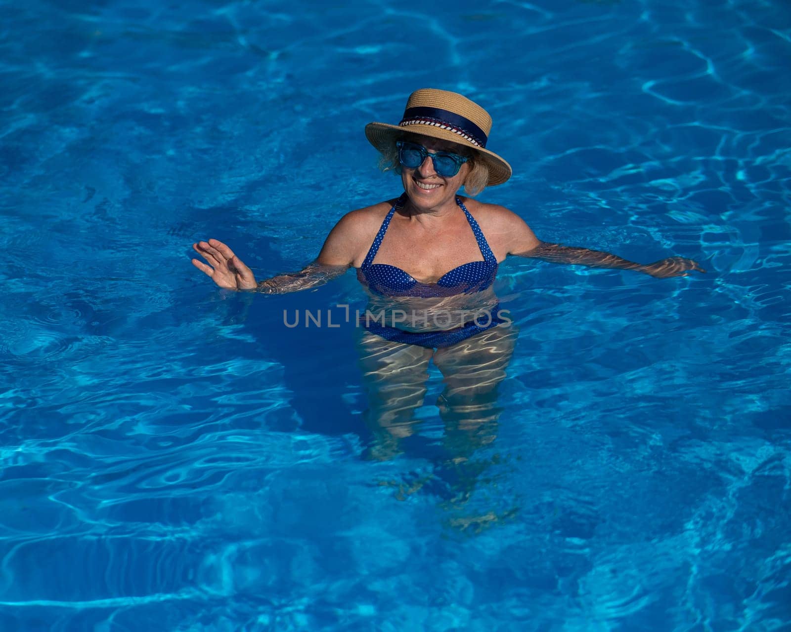 Portrait of an elderly woman in a hat and blue sunglasses swims in the pool. by mrwed54