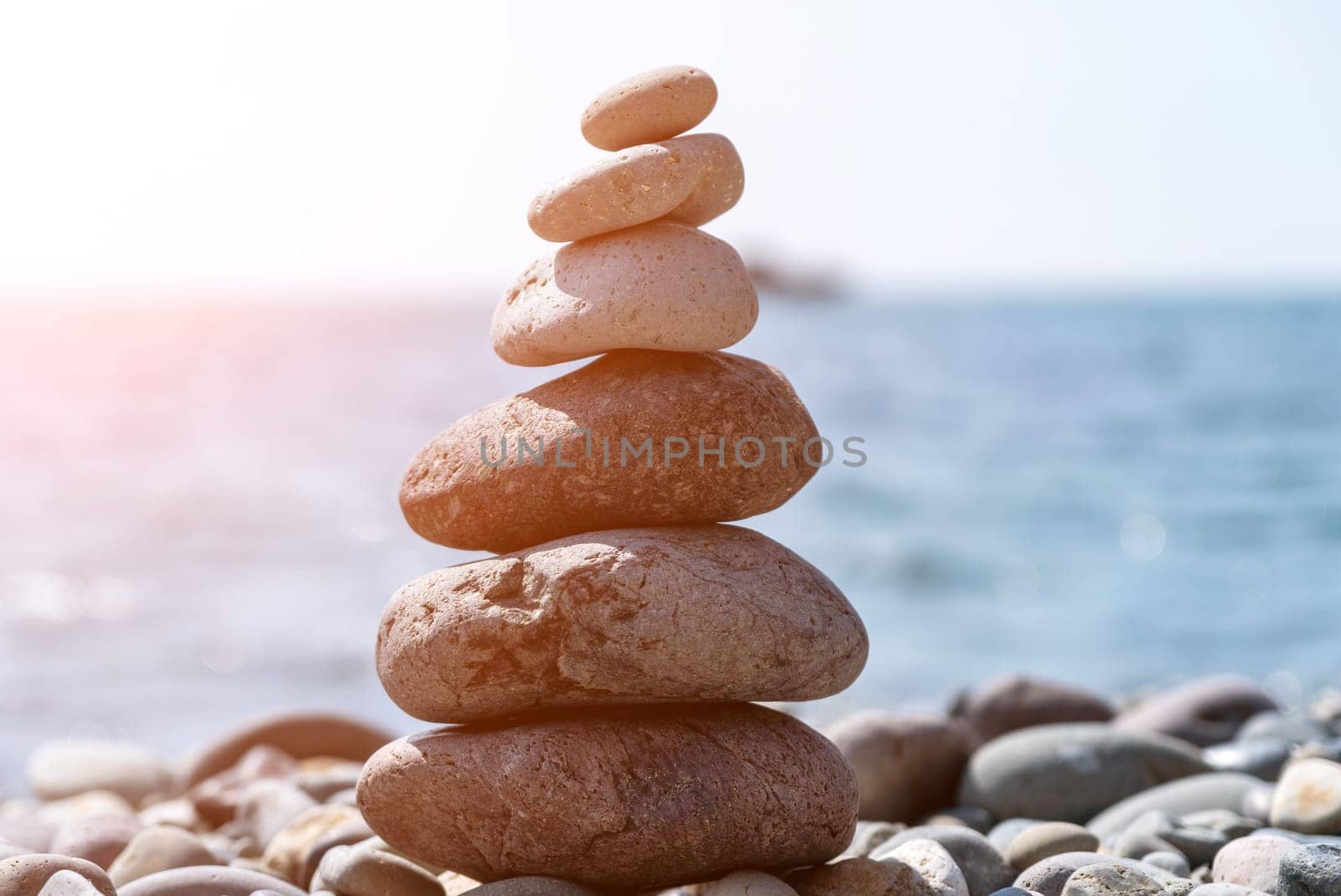 Balanced Pebbles Pyramid on the Beach on Sunny Day and Clear Sky at Sunset. Blue Sea on Background Selective focus, zen stones on sea beach, meditation, spa, harmony, calm, balance concept.