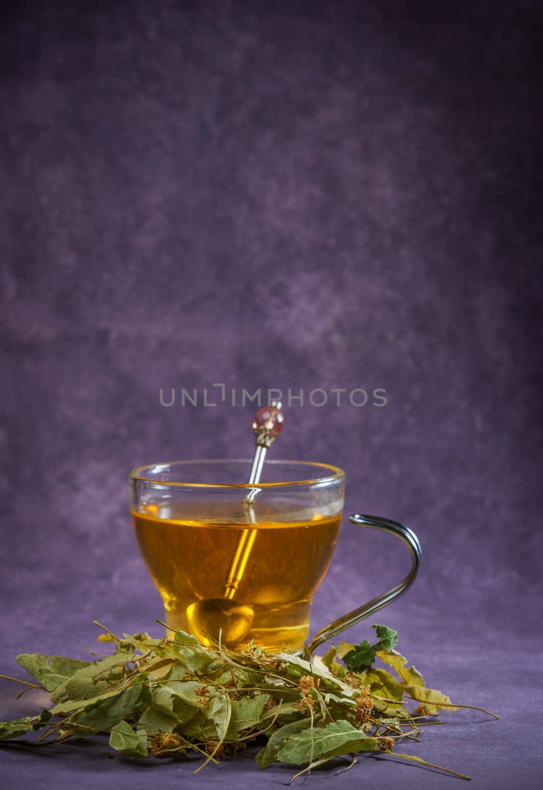 glass cup with an infusion of lime blossom tea with fresh leaves around it