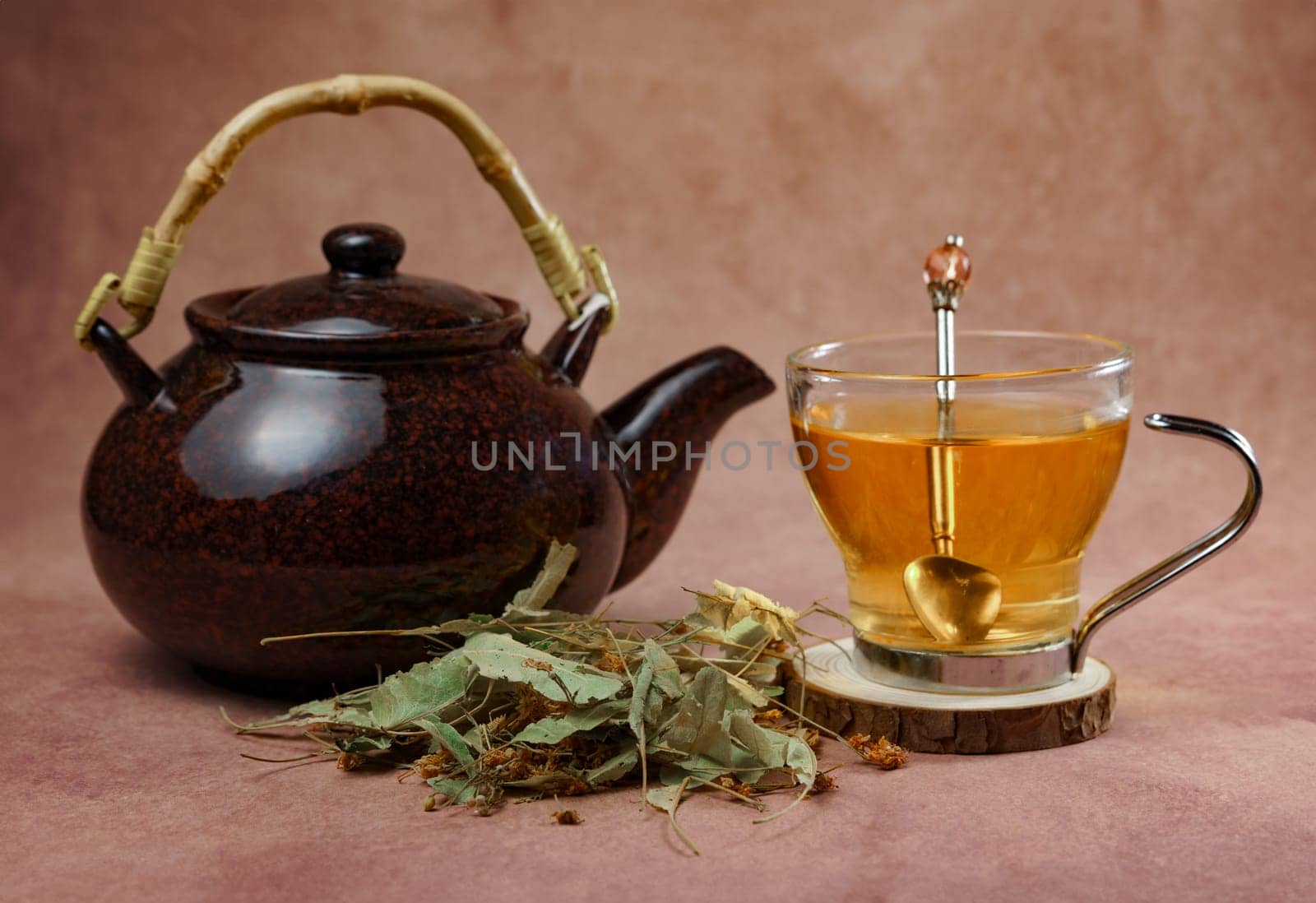 glass cup with teapot and fresh linden leaves, infusion of lime blossom tea, medicinal plant with therapeutic properties.