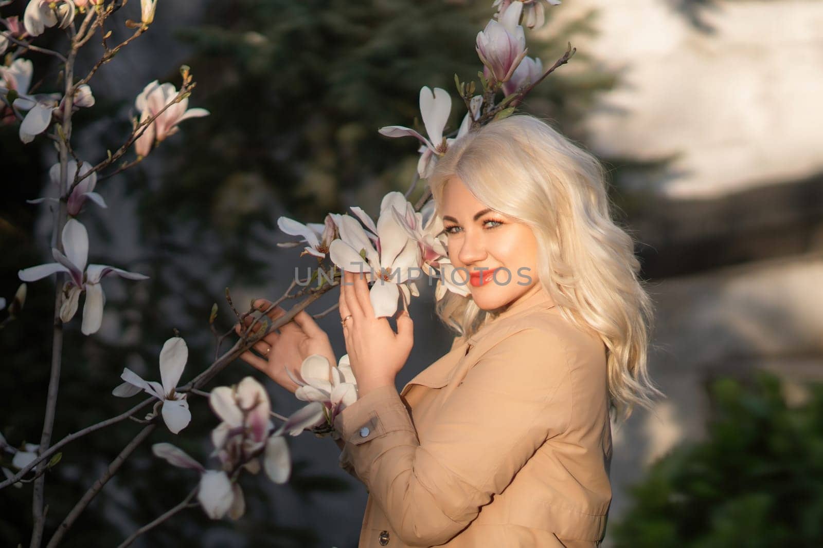 A woman is holding a magnolia flower in her hand and standing in front of a tree. Concept of serenity and beauty, as the woman is surrounded by nature and the flower adds a touch of color