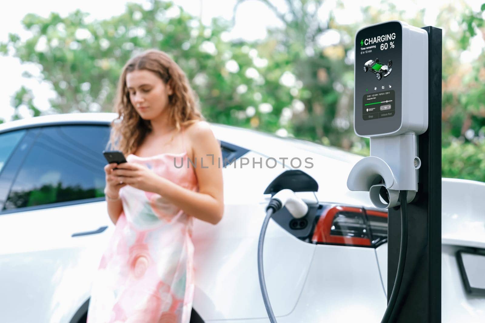 Modern eco woman recharge EV car with smartphone. Synchronos by biancoblue