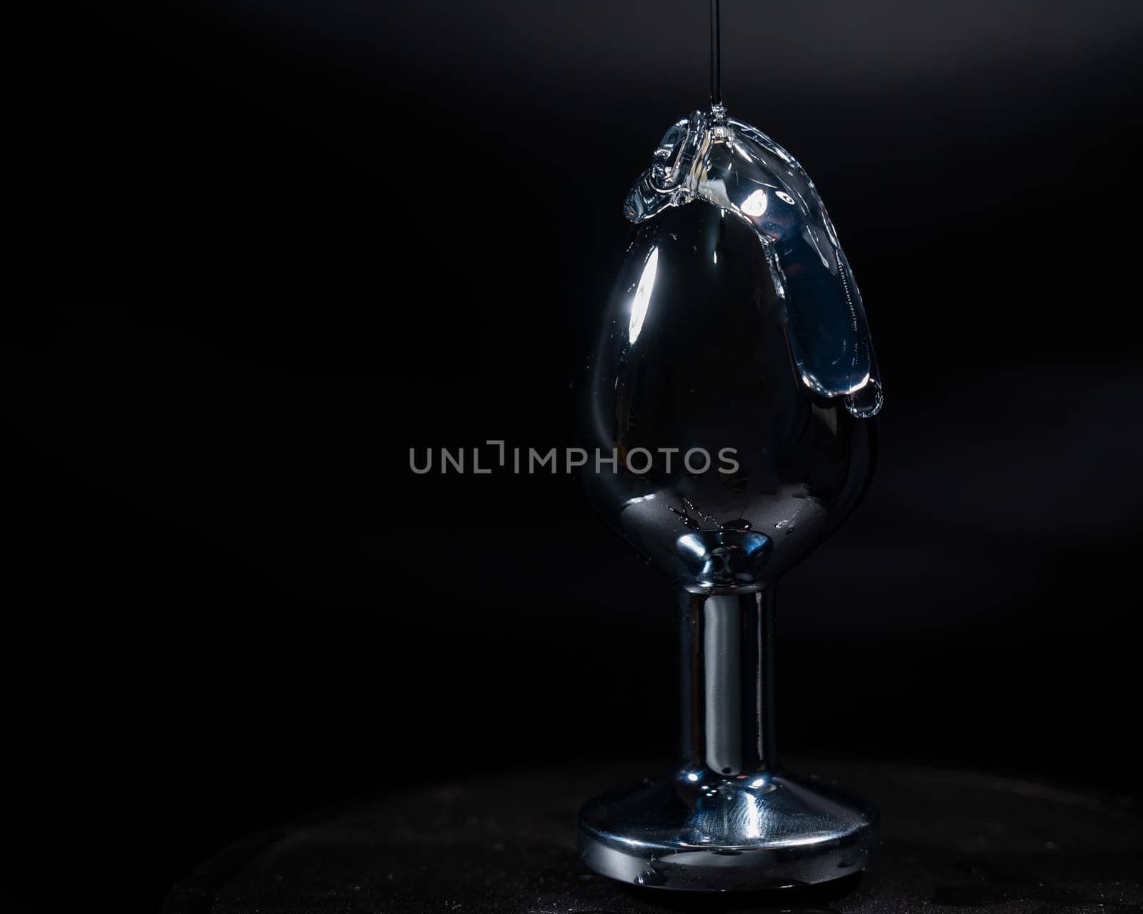 Intimate lubricant is poured onto a steel anal plug on a black background. by mrwed54
