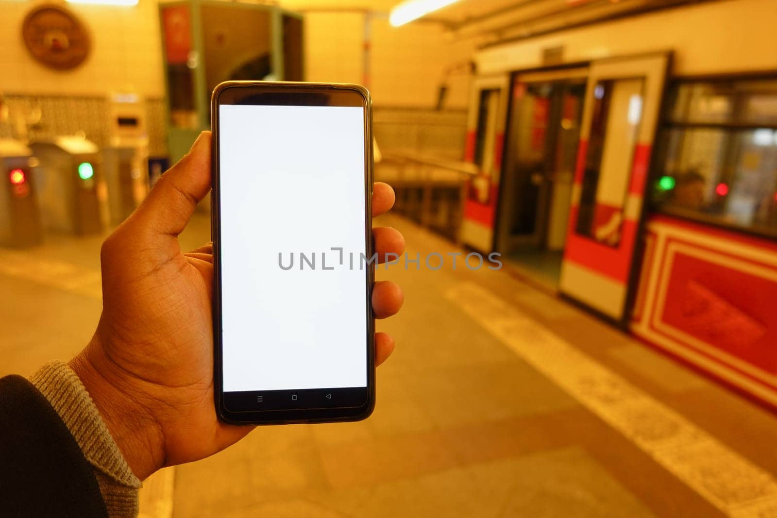 young man hand using smart phone with white screen inside of metro station .