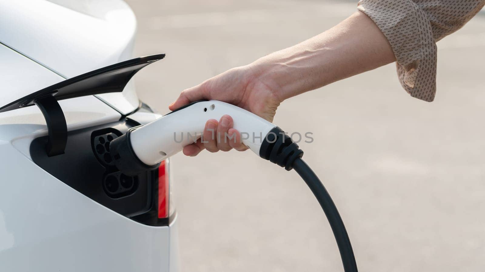 Closeup hand put EV charger to recharge electric car's battery from charging station in city commercial parking lot. Rechargeable EV car for sustainable environmental friendly urban travel. Expedient