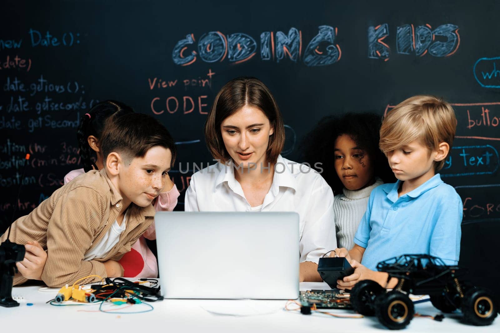 Teacher coding to demonstrate children how to code robots in the STEM class. Children fun to watch how teacher coding with confident only boy in blue shirt taking note with serious look. Erudition.