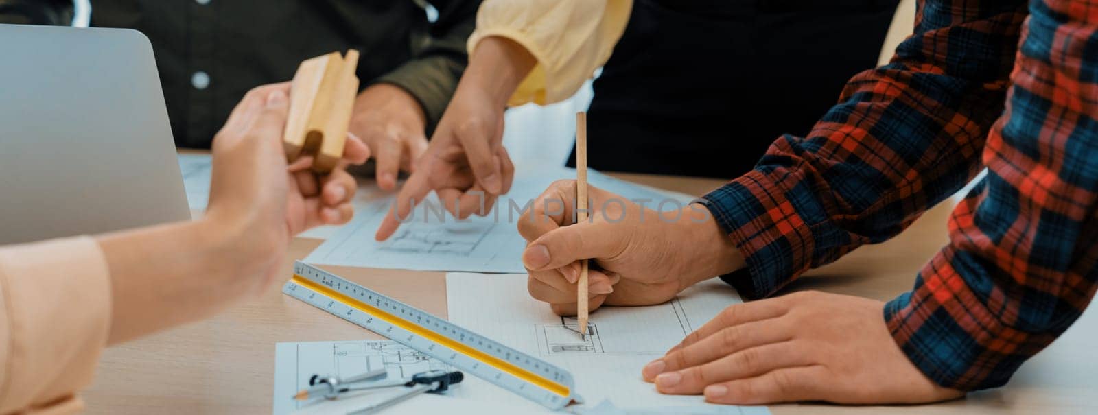 Professional architect team discussion about architectural project on meeting table with blueprint and wooden block scatter around at modern office. Closeup. Focus on hand. Delineation.