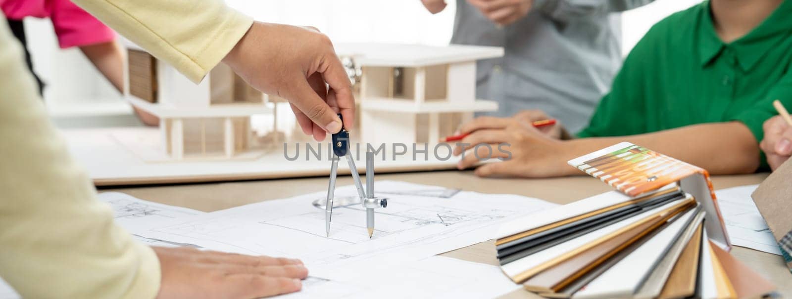 Professional architect team select sustainable house materials while skilled engineer using divider measure blueprint with house model and color palette placed on meeting table. Closeup. Variegated.