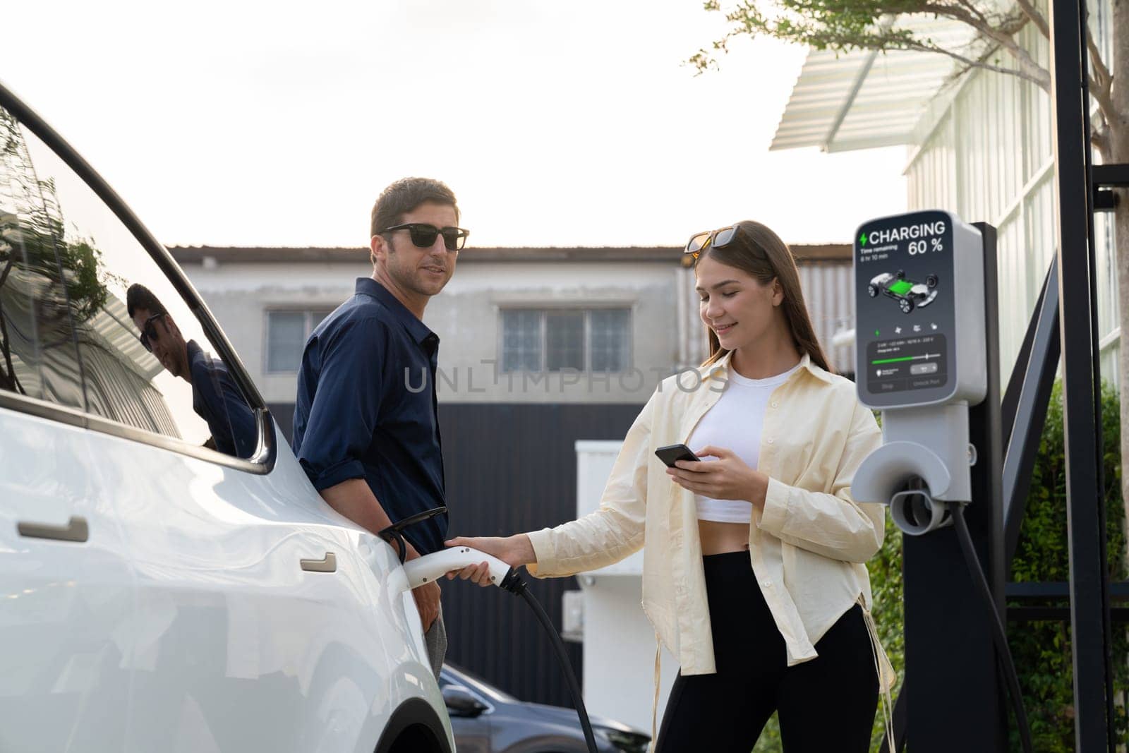 Eco-friendly conscious family couple recharging EV vehicle from home charging station. EV electric car technology utilized as alternative transportation for future sustainability. Expedient