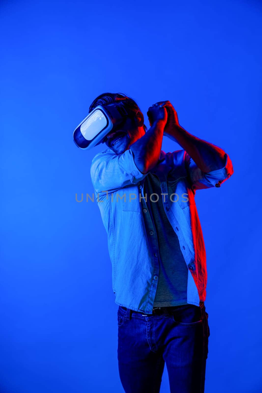 Caucasian man with VR glasses equipment moving in golf playing gesture while standing at neon background. Professional gamer enter in virtual world with futuristic technology innovation. Deviation.