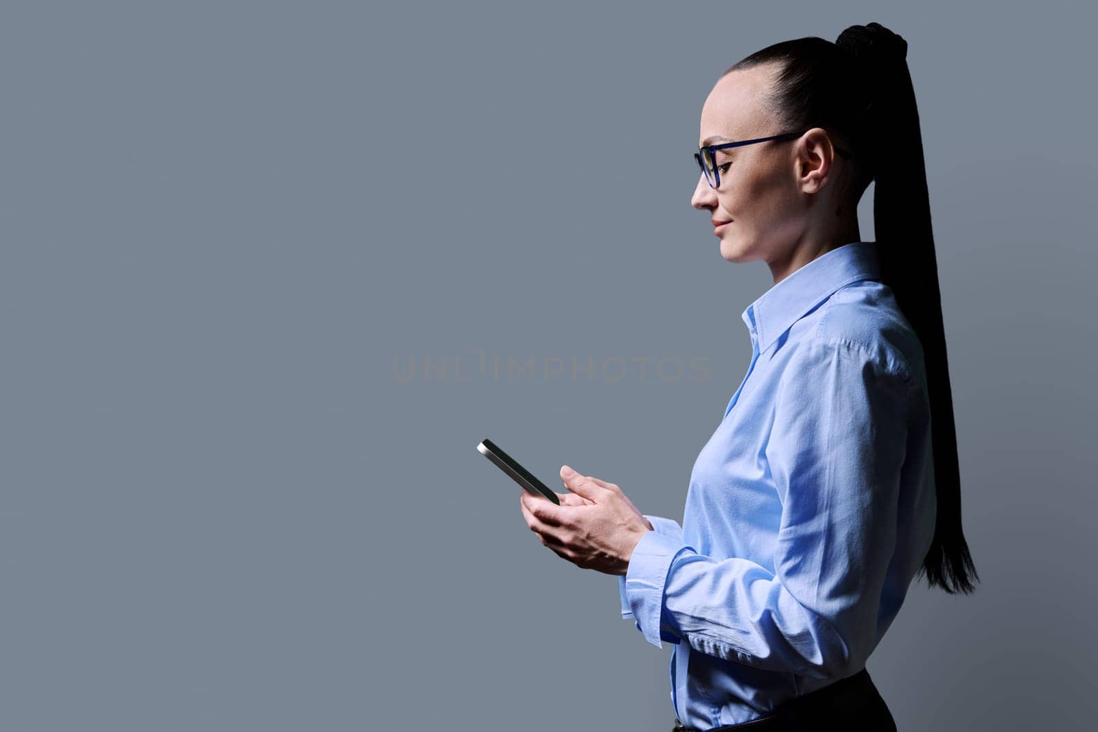Profile view 30s woman using smartphone on grey background by VH-studio