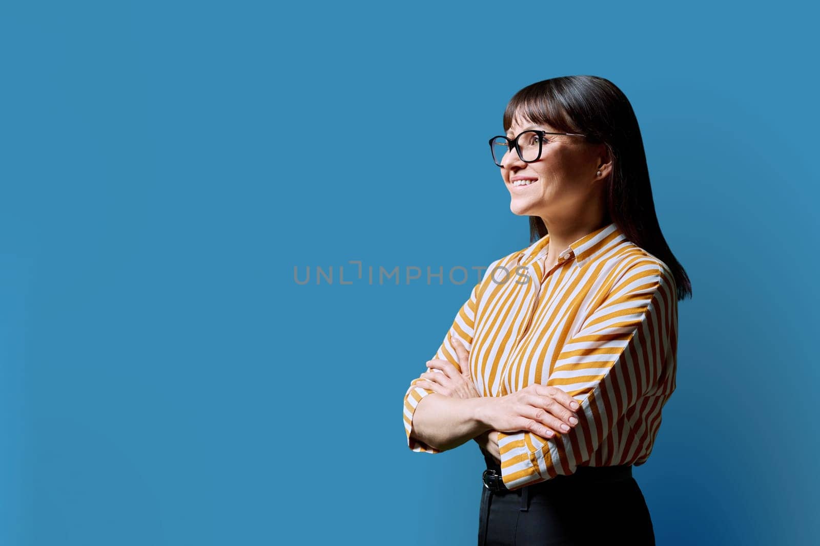 Profile portrait of mature confident smiling woman on blue studio background. Middle-aged happy female looking to side, copy space for advertising text image. Business work services education health