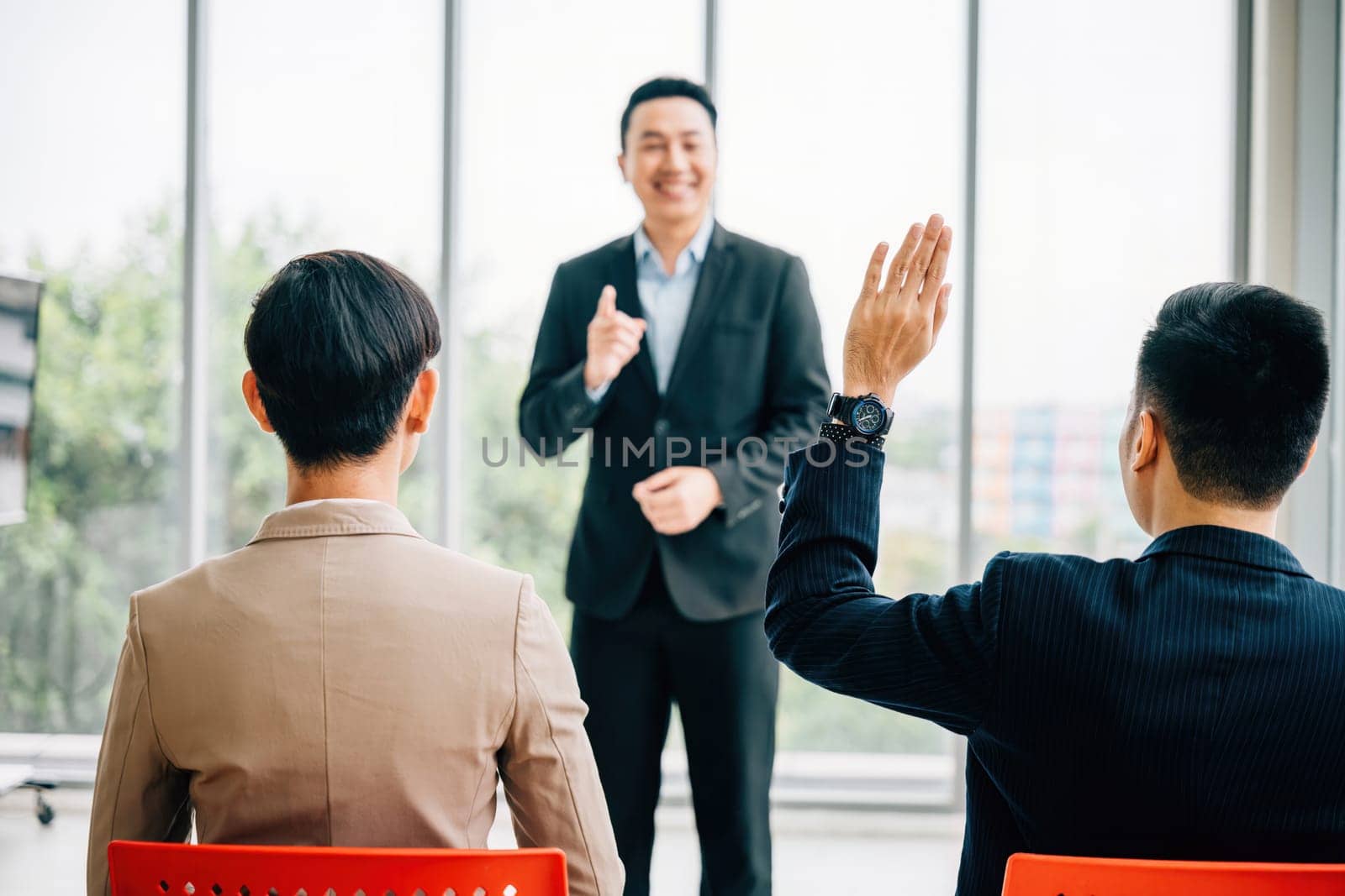 At a corporate event, a diverse audience of businesspeople raises their hands for questions, voting, or volunteering. The scene highlights teamwork and interactive audience participation.