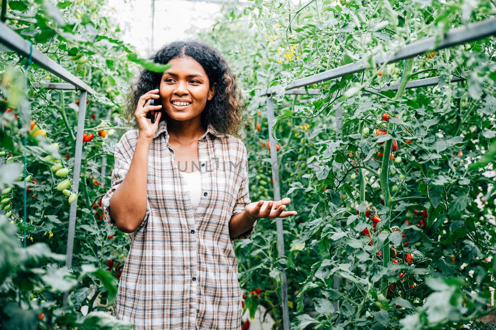 Woman farmer in greenhouse talks on phone by Sorapop