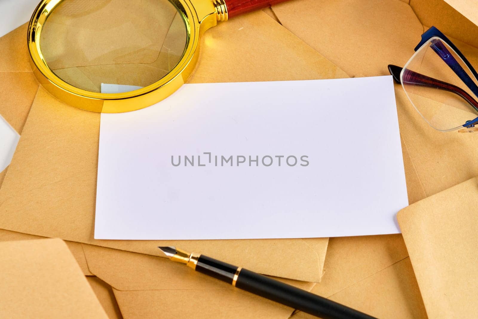 A blank sheet on the envelopes next to a pen, glasses and a magnifying glass