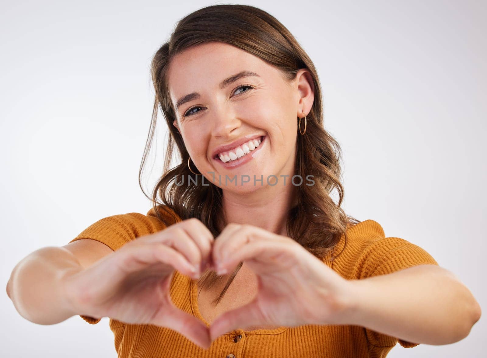 Happy woman, portrait and heart hands with love in care, romance or kindness on a gray studio background. Young female person with smile for shape, like emoji or support for review, gesture or symbol by YuriArcurs