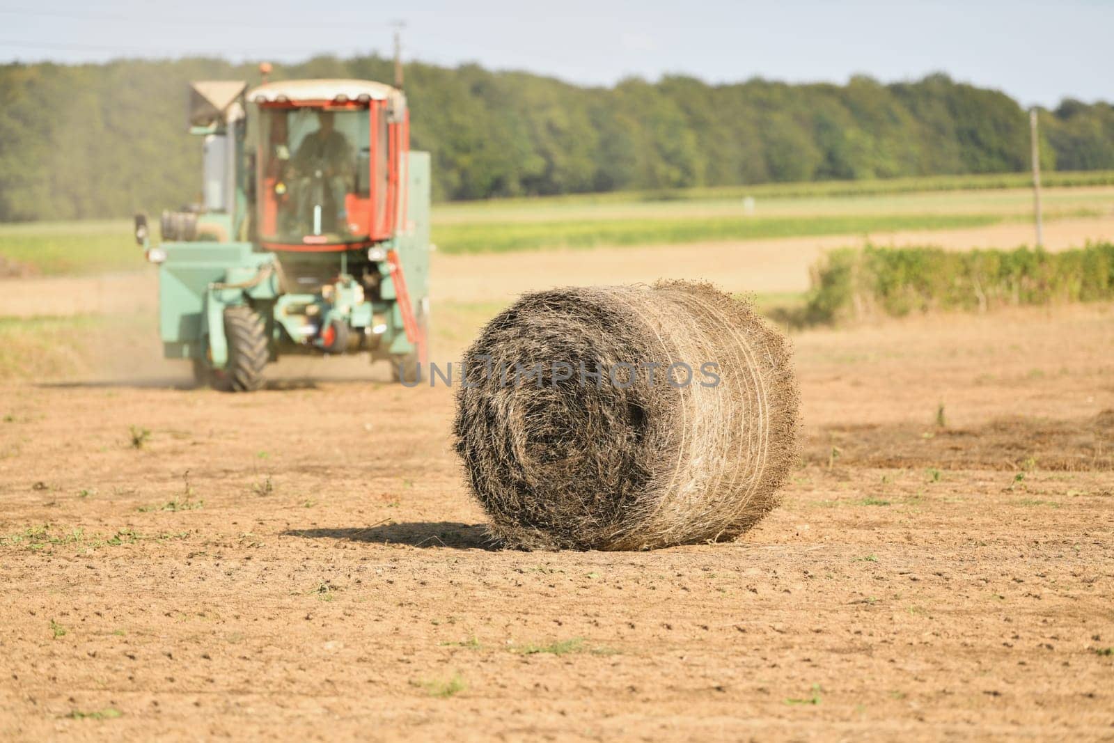 A tractor cleans the field with flax and makes bales by Godi