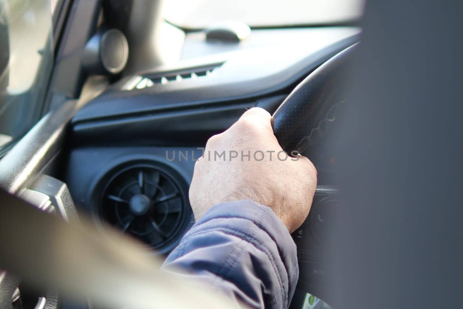 A man is driving a personal luxury car, his hand placed on the steering wheel, controlling the vehicles movement with a confident gesture
