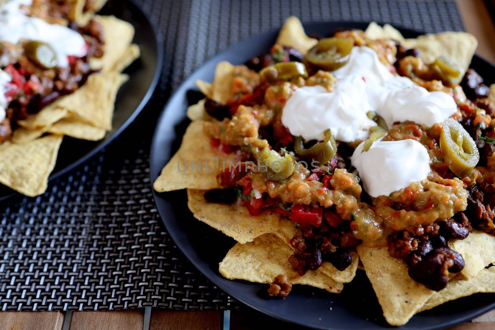 Appetizing dish on a plate: corn chips nachos with fried minced meat and guacamole, beans, salsa, jalapenos top view. Homemade Mexican cuisine
