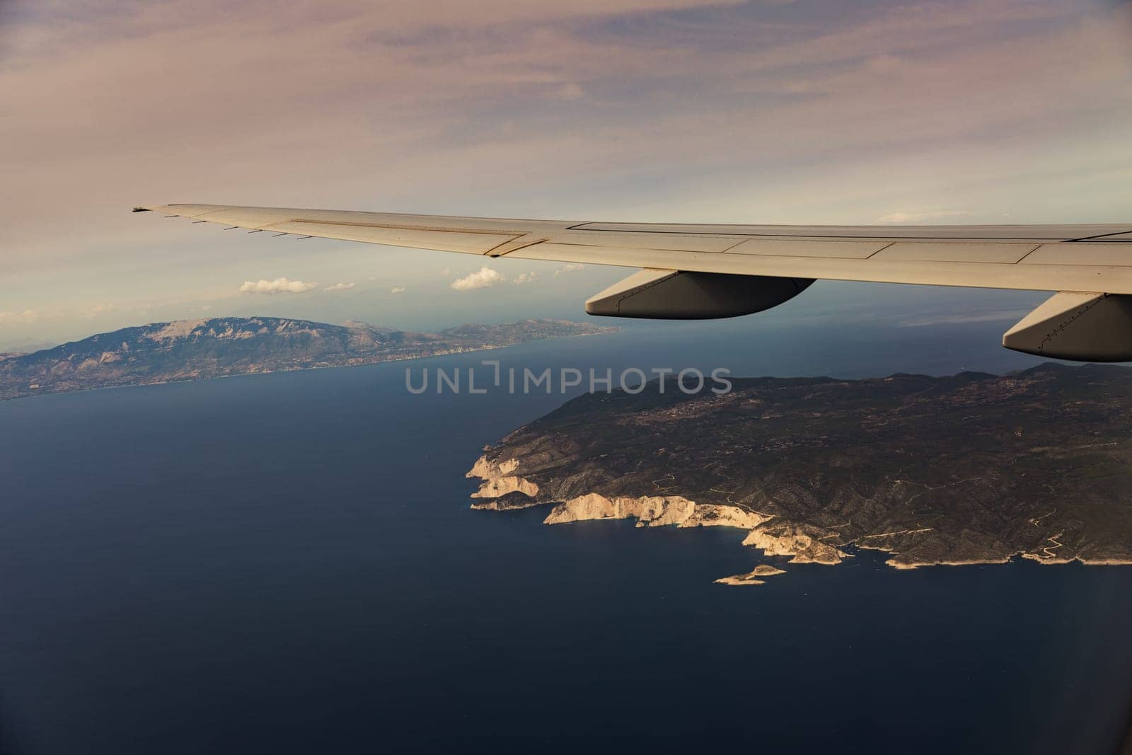 A beautiful view of the wing of an airplane and an island in the sea through the porthole window from the height of an airplane in the evening at sunset, close-up side view.