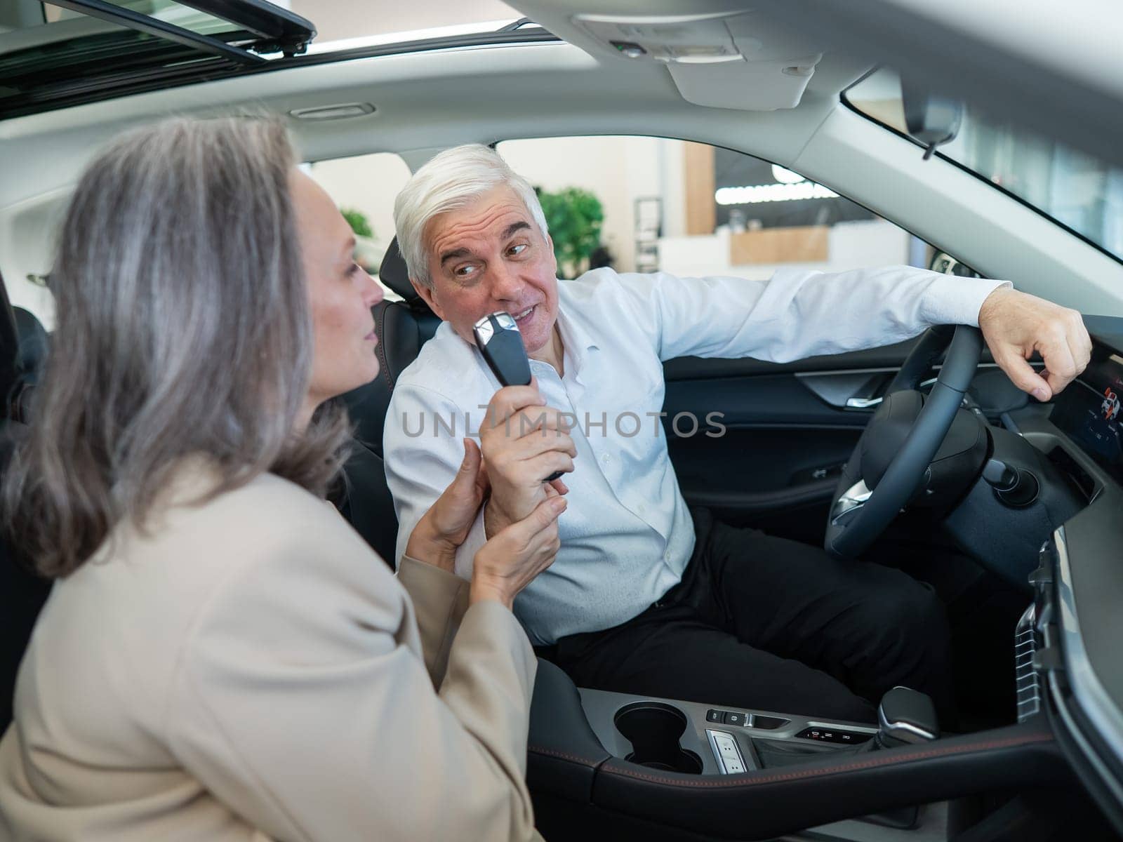 Mature Caucasian couple sitting in a new car and rejoicing at the purchase. by mrwed54