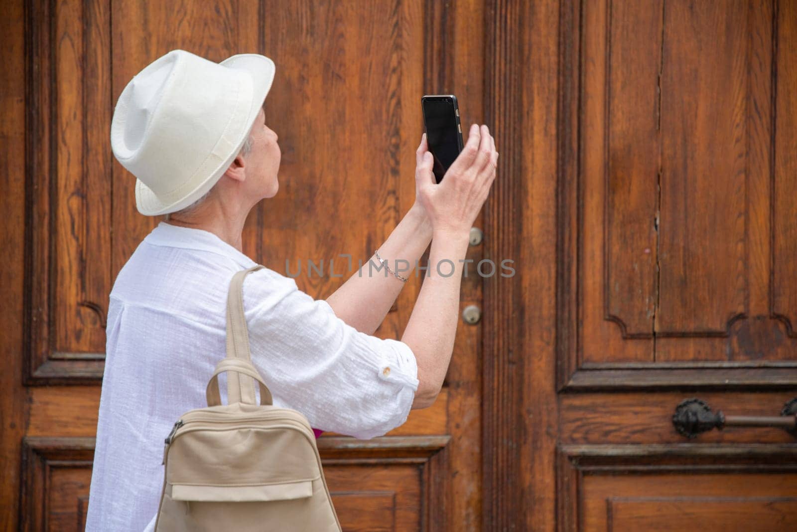elderly stylish female tourist taking photo of textured wooden door, active lifestyle and use of technology at age by KaterinaDalemans