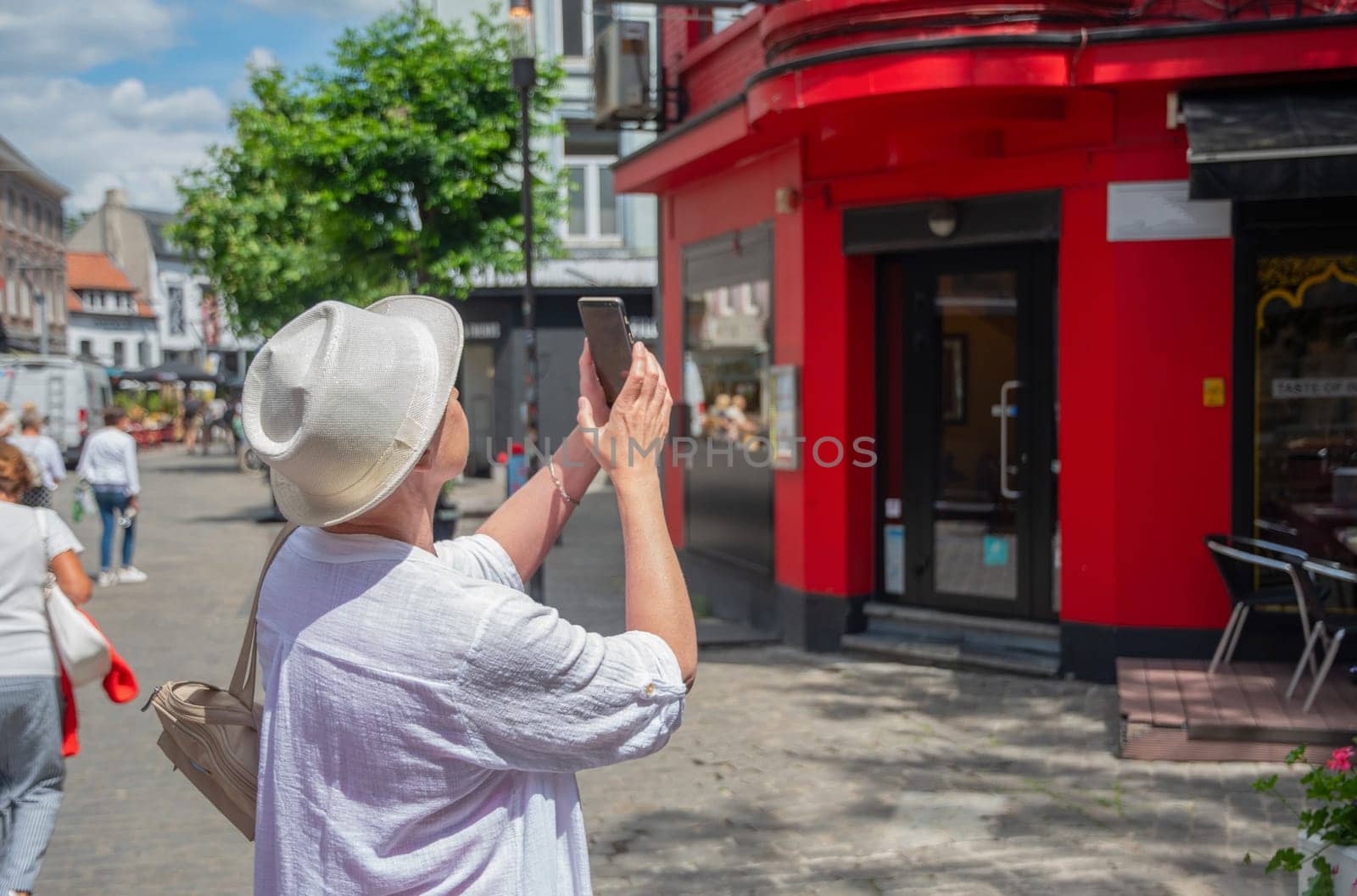 elderly stylish female tourist taking photographs of a unique red house on a city street, active lifestyle and use of technology at age, high quality photo