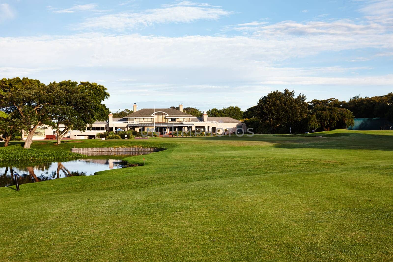 Grass, sky and trees on golf course with building, lake and natural landscape with park in summer. Nature, green and field with water at sports club with sustainable environment in outdoor sunshine.