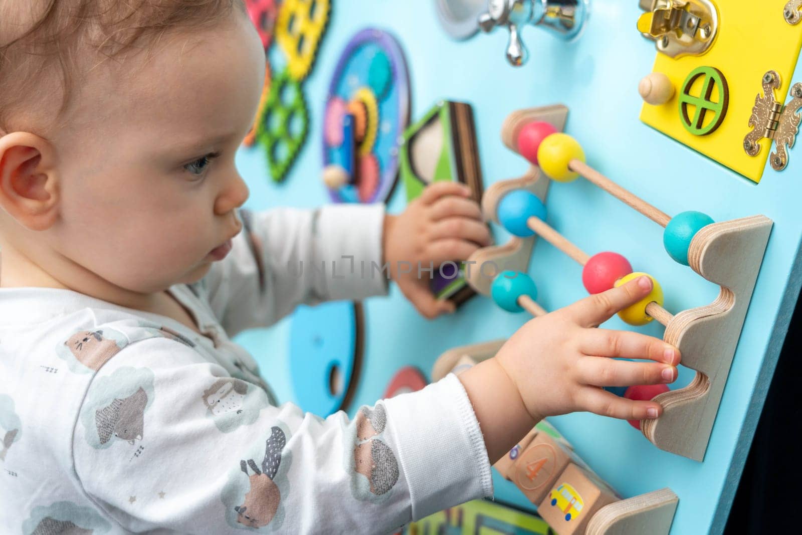 Close-up of a cute kid moving with concentration round colored wooden elements on a busy board.