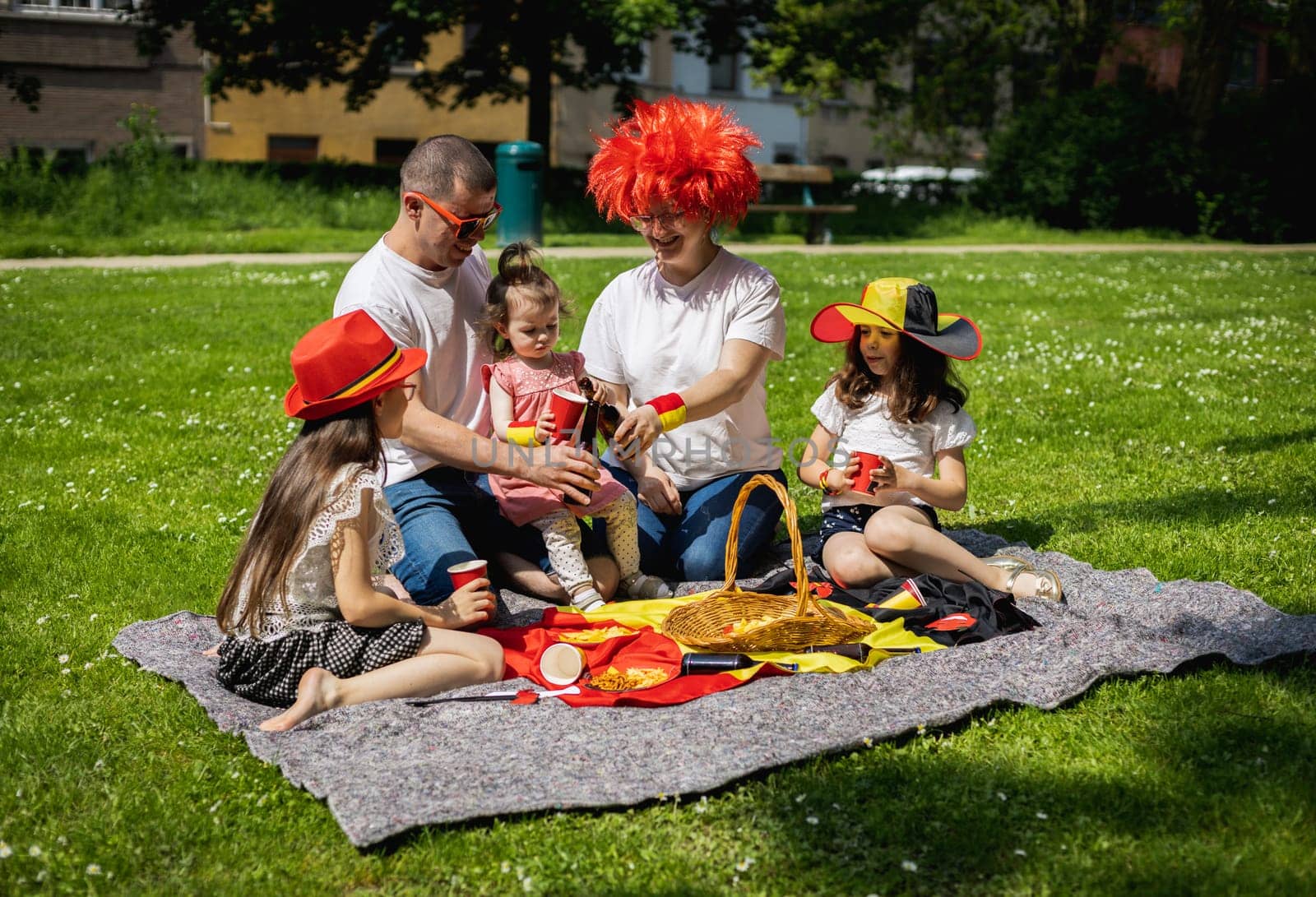 Portrait of beautiful and happy caucasian parents with three children girls celebrating belgium day at a picnic in a city park on a sunny summer day, side view close up.